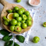 Close-up of fresh green plums, lemon, and salt on a table with leaves, depicting a traditional Turkish snack.