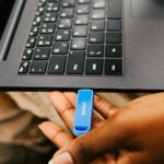 A hand inserting a blue usb drive into a laptop.
