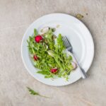 Healthy arugula and radish salad with seeds on white plate viewed from above.