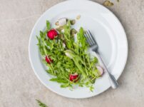 Healthy arugula and radish salad with seeds on white plate viewed from above.