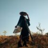 Stylish woman holds a fan in a desert setting, exuding elegance and mystery.