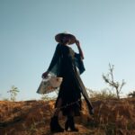 Stylish woman holds a fan in a desert setting, exuding elegance and mystery.