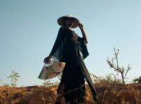 Stylish woman holds a fan in a desert setting, exuding elegance and mystery.