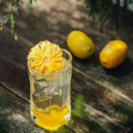 A cool citrus beverage with ice and a dried citrus garnish, set outdoors on a rustic wooden table.