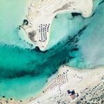 Stunning aerial photograph of Elafonissi Beach, showcasing turquoise waters, sandy shores, and sun umbrellas.