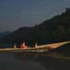 Two people with dogs travel on a wooden canoe in the Amazon River, Peru.