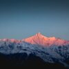 A breathtaking view of snow-covered Himalayan mountains under a vibrant sunrise with pink hues.