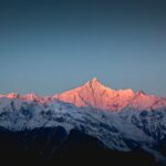 A breathtaking view of snow-covered Himalayan mountains under a vibrant sunrise with pink hues.
