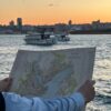 Person holding a map of Constantinople with boats and a city skyline at sunset on the Bosphorus.
