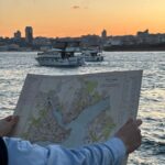 Person holding a map of Constantinople with boats and a city skyline at sunset on the Bosphorus.