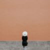 A minimalistic photo of a person in a hat against a large orange wall, perfect for design needs.