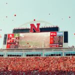Fans celebrate at a football stadium with scoreboards.