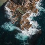 Aerial view of an ocean pool surrounded by crashing waves.