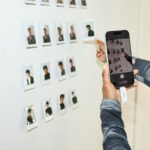 Person photographs small pictures on a white wall with phone.