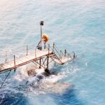 A wooden pier extends into the blue ocean with waves.