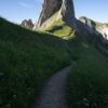 A winding path leads through green mountains to jagged peaks.